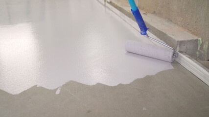 A worker paints the concrete floor with white paint. A worker paints the floor with a roller....