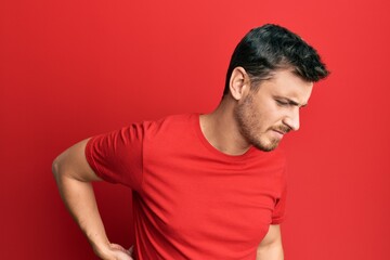 Handsome caucasian man wearing casual red tshirt suffering of backache, touching back with hand, muscular pain