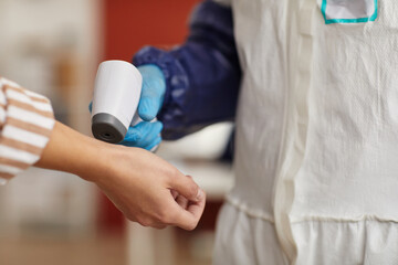 Close up of unrecognizable medical worker checking temperature with contactless thermometer pointing at female hands, copy space