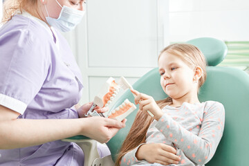 Dentist teaching girl how to brush teeth. Pediatric dentist educating a child about tooth-brushing on a model.