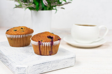 Delicious muffins with black currants close-up on a white wooden board on the background of a cup. Selective focus.