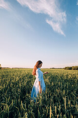 A young woman standing in a wheat field at sunset