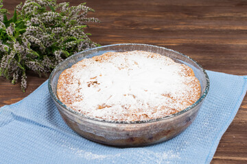 Freshly baked apple pie in a glass dish sprinkled with powdered sugar on a wooden dark background.