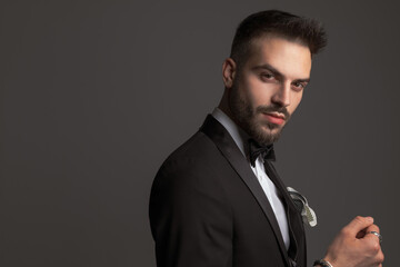 Fototapeta premium side view of attractive groom in black tuxedo posing