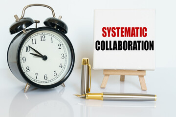 On the table there is a clock, a pen and a stand with a card on which the text is written - SYSTEMATIC COLLABORATION