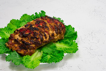 A large piece of chopped pork meat, cooked in the oven, baked in the oven, on green lettuce leaves, close-up.