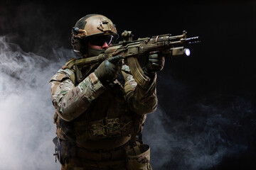Side view of army soldier in military camouflage uniform, helmet, glasses and mask holds rifle near...
