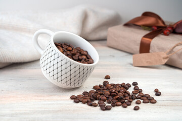 Coffee Cup with coffee beans tilted on a light background with a sweater and gift box. Side view.