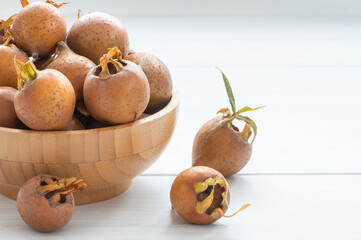 Fresh ripe organic common medlar fruit in plate or bowl on wooden rustic background. Healthy food Mespilus germanica