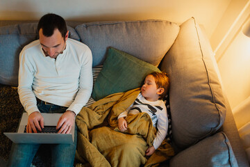 Father using laptop in living room while daughter sleeping next to him, Sweden