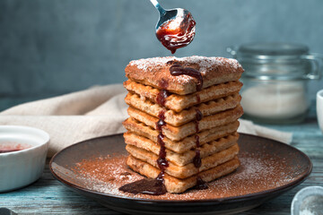 Heart-shaped Viennese waffles with chocolate, powdered sugar and strawberry sauce on a grey background. Side view. The concept of desserts.