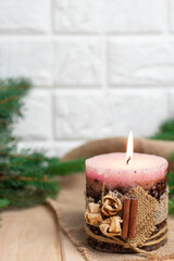 Decorated burning candle on a wooden background with a brick wall. Festive mood. Vertical orientation.