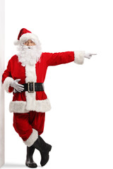 Full length portrait of santa claus leaning on a wall and pointing to the side