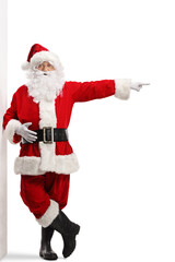 Full length portrait of santa claus leaning on a wall and pointing to the side