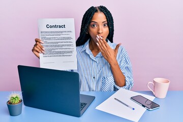 Beautiful hispanic woman at the office showing contract document covering mouth with hand, shocked...