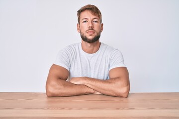 Young caucasian man wearing casual clothes sitting on the table with serious expression on face....