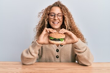 Beautiful caucasian teenager girl eating a tasty classic burger winking looking at the camera with...