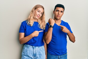 Young interracial couple wearing casual clothes in hurry pointing to watch time, impatience,...