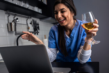Young female nurse at home in the kitchen having video call using laptop.