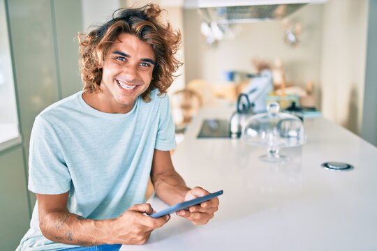 Young hispanic man smiling happy using touchpad sitting on the table at home