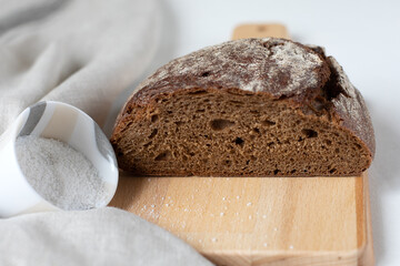 Cut black rye bread with salt on a wooden board on a light background