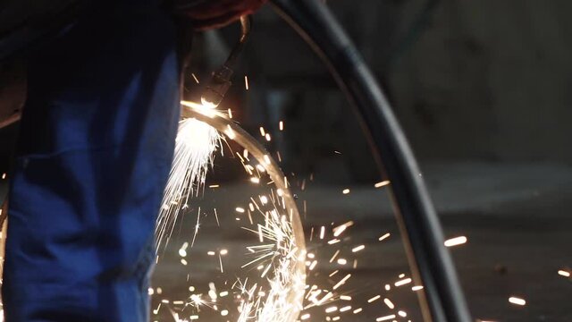 A man cuts a pipe with flame cutting torch to sparks in a workshop, slow motion