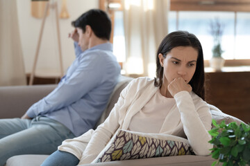 Too far from one another. Nervous angry young couple sitting on opposite sides of sofa keeping...