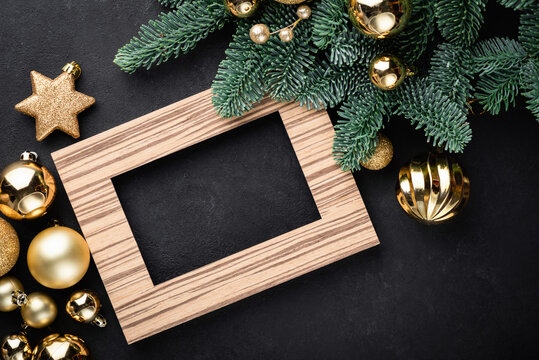 Christmas or New Year background with empty photo frame, fir tree and golden Christmas toys on black background