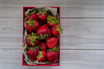 box full of delicious bright red strawberries on a beige wooden table