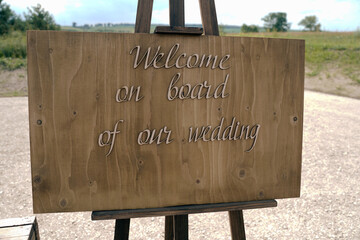 Welcome on board of our wedding. Easel with a wooden board and an inscription for guests on the wedding day