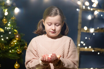 Beautiful little girl holding Christmas lights in magic holiday lights on Christmas Eve.