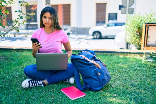 Young latin student girl smiling happy using smartphone and laptop at university campus.