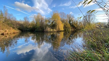 Park canal in a beautiful sunny autumn day with trees and cloud reflecting on the calm, still water, scenic nature landscape, beautiful nature, blue sky and water.