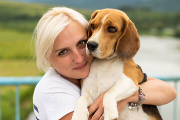 Cute woman close up portrait, hugging beagle dog at the walk. Smiling young woman enjoying good day and posing with pet. Real people concept.