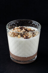 Layered gourmet dessert in a glass: vanilla and chocolate panna cotta on a black background