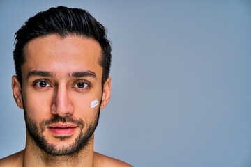 Obraz premium Closeup positive guy with a black beard with white spot of cream on his cheek. Cosmetics concept