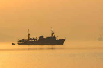 Silhouette of the ship in the morning at dawn in the fog. The Eastern Bosphorus strait between Tokarevsky lighthouse and the Russian island in Vladivostok.