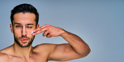 Closeup guy with beard with fun applying white cream on his cheek by fingers. Cosmetics concept