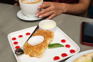 a piece of Napoleon cake decorated with drops of jam and the hands of a girl holding coffee, slice of pie with ice cream and the hands of a girl holding a cup of cappuccino