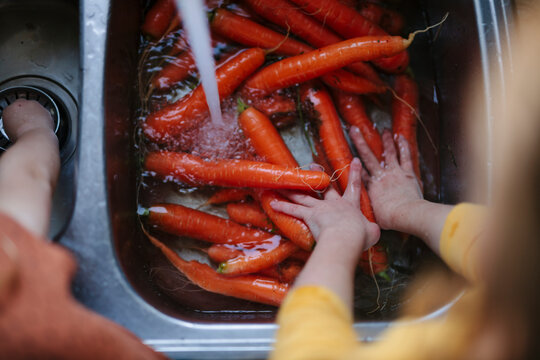 Girl washing carrots in kitchen sink, Sweden