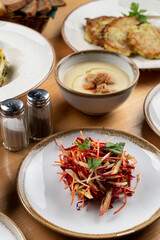 Grated vegetable salad with carrot, raw beetroot and cabbage, side view on wooden table with meals on background