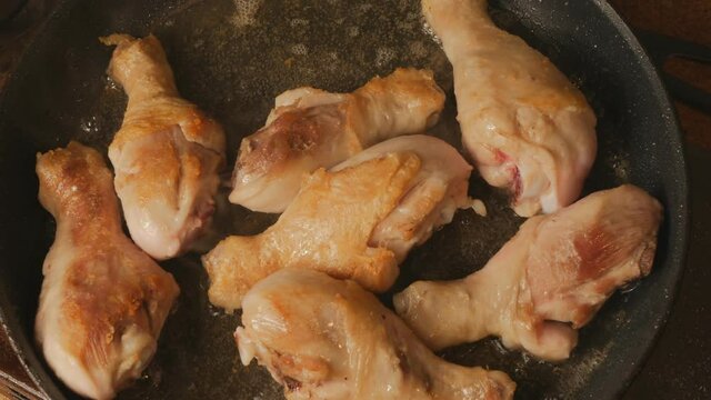 chicken legs are fried in a large skillet in vegetable oil. Top view of grilled poultry meat in a frying pan. Fatty fried foods cause heart disease