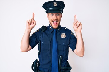Young caucasian man wearing police uniform smiling amazed and surprised and pointing up with fingers and raised arms.