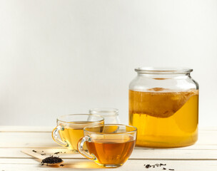 Two cups of tonic fermented Kombucha drink and a jug of growing zooglea, on a light background with space