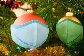 Two Christmas ball wearing cloth face masks. Safely celebrating the winter holidays during the coronavirus pandemic.