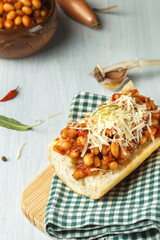 baguette with baked beans and grated cheddar on a green checkered napkin, close-up on a light wooden background