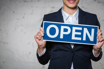 Midsection of young businesswoman holding open sign placard against brick wall