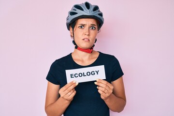 Beautiful caucasian woman wearing bike helmet holding ecology word clueless and confused expression. doubt concept.