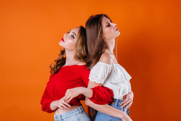 Two young and beautiful girls shows emotions and smiles in the Studio on an orange background. Girls for advertising