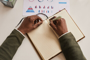 Top view close up of unrecognizable man writing in planner while working at desk in office, focus...